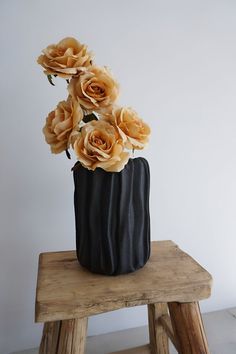 there is a black vase with flowers in it on a small stool next to a white wall