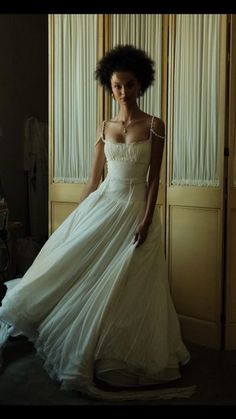 a woman in a white dress is standing near a door and posing for the camera