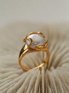 The Flower Bud Baroque Pearl Ring combines simplicity and elegance with its natural coin-shaped baroque pearl and clean metal design. The high-luster pearl is securely set in claw prongs, resembling a blooming flower bud, and paired with a sleek, polished band. This adjustable open ring is available in gold or silver tones, offering versatility to suit any finger size and style. Perfect for a chic, modern look that complements any outfit. Product Details Material: Copper with Gold or Silver Plat Unique Pearl Rings, Pearl Rings In Gold, Pearl Engagement Ring Vintage, Baroque Jewelry, Pearls Ring, Blossoming Flower, Pearl Diamond Ring, Pearl Rings Vintage, Natural Buttons