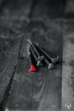 several black and red matchesticks laying on top of a wooden table next to a heart