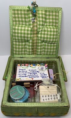 an open green suitcase filled with lots of items on top of a white tablecloth covered floor