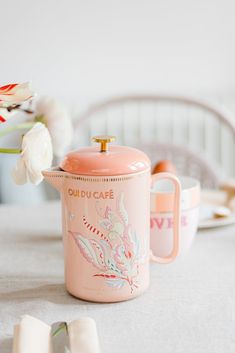 a pink coffee pot sitting on top of a table next to two napkins and a vase