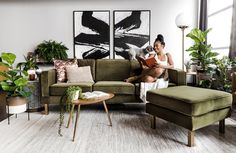 a woman sitting on a couch reading a book in her living room with potted plants