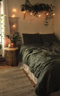 a bed with green sheets and pillows in a bedroom next to a window filled with potted plants