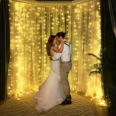 a bride and groom standing in front of a curtain with lights on it at their wedding reception