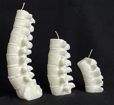 three white candles shaped to look like toothpicks on a black background with one candle in the shape of a human's mouth