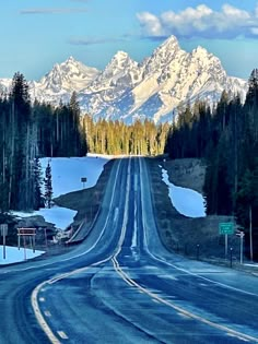 an empty road in front of mountains with snow on the ground and trees around it