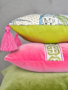 two pillows with tassels are stacked on top of each other, one pink and the other green