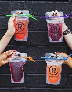 three people holding up plastic cups with liquid in them and straws hanging from the handles