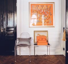 an orange painting hangs on the wall next to a clear chair in front of a black door