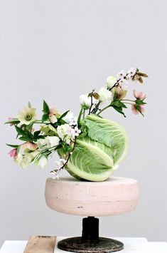 a vase with flowers in it sitting on top of a white table next to a piece of wood