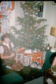 a woman sitting in front of a christmas tree with presents on the floor next to it