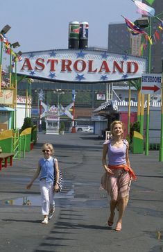 two girls are walking down the street in front of an astroland sign and amusement park