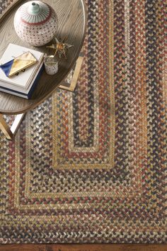 a table with a vase and books on it next to a rug that is multicolored