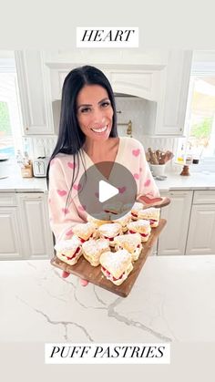 a woman holding a tray full of pastries on top of a kitchen countertop