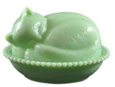 a small green bowl with a cat on it's side and pearls around the rim