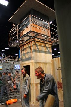 two men standing next to each other in front of a fenced area with a tower