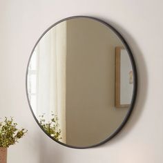 a round mirror hanging on the wall above a table with a potted plant next to it