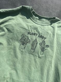 Channel your inner green thumb with our Plant Lady Tee. Made from soft, organic cotton, this shirt worn proudly displays your love for all things botanical. Perfect for brunch, gardening, or just lounging in the sun. Embrace your plant obsession in style. (Gardening gloves not included!) Plant Shopping Outfit, Fall Merch, Plant Obsession, Merch Ideas, Market Ideas, Botanical Shirt, Gardening Shirts, Gardening Gloves, Plant Lady