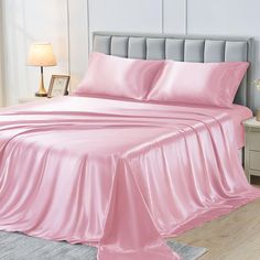 a bed with pink sheets and pillows on top of it in a room next to a lamp