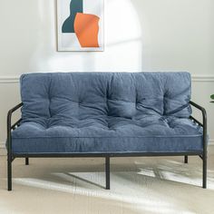 a blue futon sofa sitting on top of a hard wood floor next to a plant