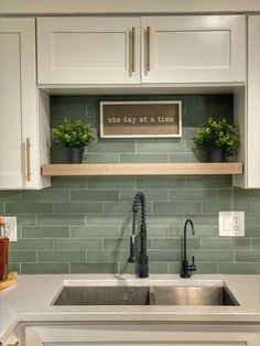 a kitchen with white cabinets and green tile on the backsplash, above a stainless steel sink