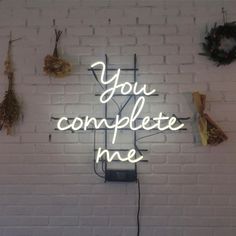 a neon sign that says you complete me on a brick wall with other items around it