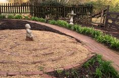 a small statue in the middle of a circular garden area with brick pavers paths