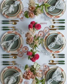 the table is set with plates, silverware and pink flowers in vases on them