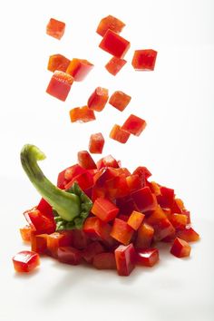 diced vegetables being tossed in the air on a white surface with one green pepper