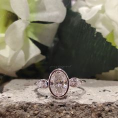 a close up of a ring on a rock with flowers in the background