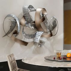 a metal sculpture sitting on top of a white table next to a glass vase filled with oranges