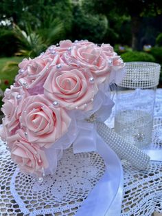 a bouquet of pink roses and pearls on a lace doily with a glass vase in the background