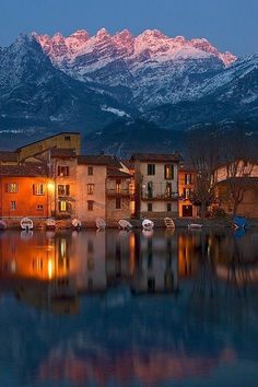 the mountains are reflected in the still water of this town's lake at dusk