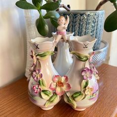 two vases with flowers and a small figurine in the middle on a table