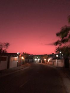 an empty street at night with lights on and trees in the foreground as the sun sets