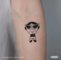 a small cartoon character tattoo on the left inner forearm and arm, with an eye patch at the center