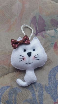 a white cat ornament with a bow on it's head is hanging from a cord