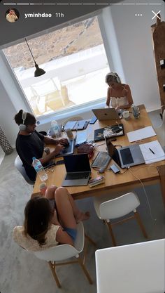 three people sitting at a table with laptops and papers in front of large windows