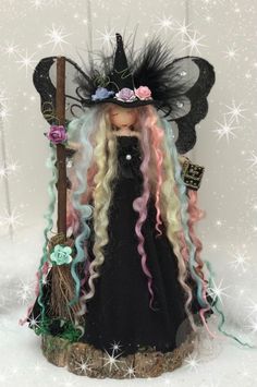 a doll with long blonde hair and a black dress holding a broom in her hand