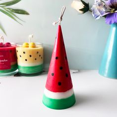 three candles are sitting on a table next to each other and one has a watermelon cone