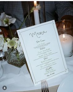 a menu sitting on top of a table next to a candle and some white flowers