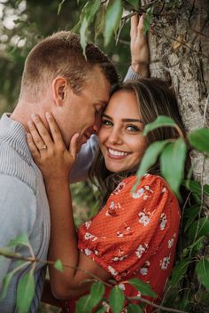 a man and woman hugging each other in front of a tree with leaves on it