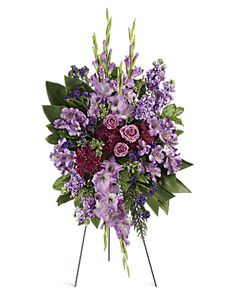 purple flowers and greenery arranged on a stand