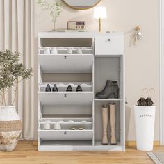 a white shoe cabinet with shoes and boots in it next to a potted plant