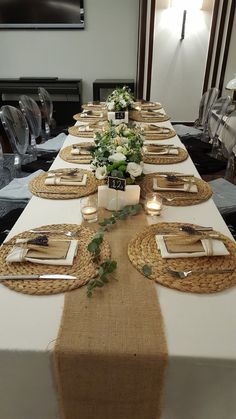 a long table set with place settings and flowers on the runner, along with candles