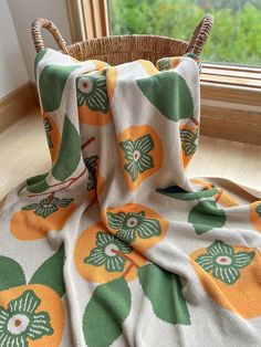 an orange and green flowered blanket sitting on top of a wooden floor next to a basket