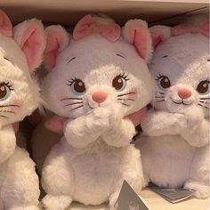 three white stuffed animals sitting next to each other on top of a shelf in a store