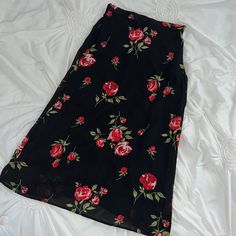 a black skirt with red roses on it laying on a white bed sheet in the sunlight