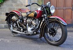 a red and black motorcycle parked in front of a building next to a wooden door